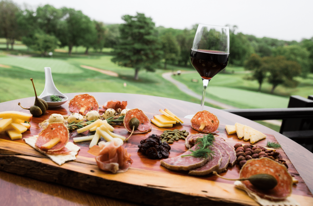 Charcuterie board outside with glass of wine overlooking golf course at Salina Country Club