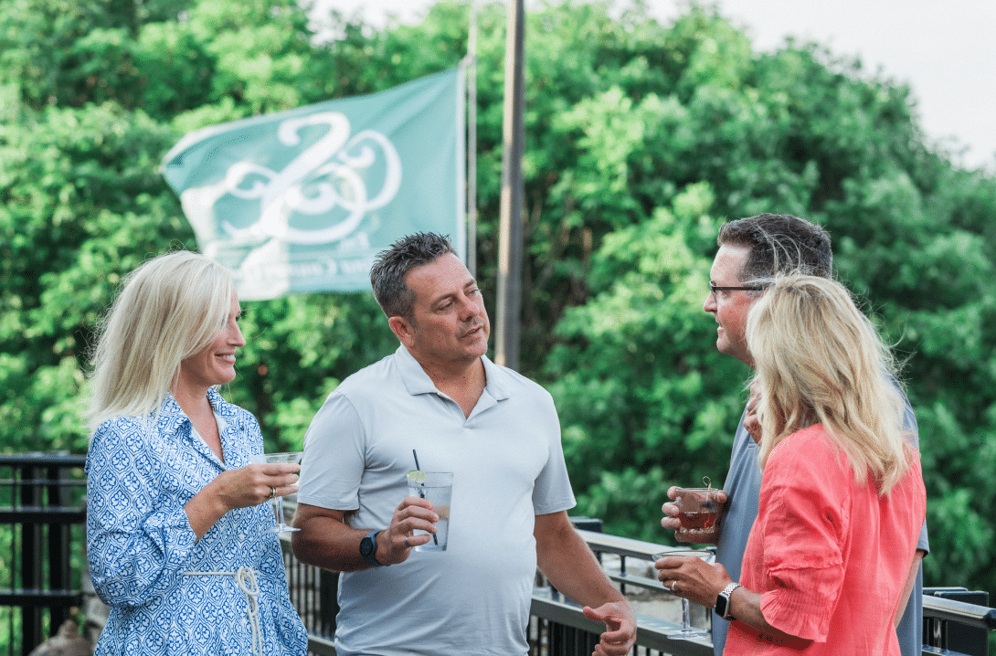 Two couples having drinks outside in front of flag with Salina Country Club logo