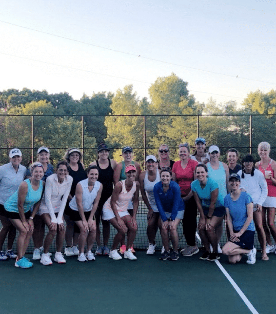 Women's tennis group gathering outside on a tennis court for a photo