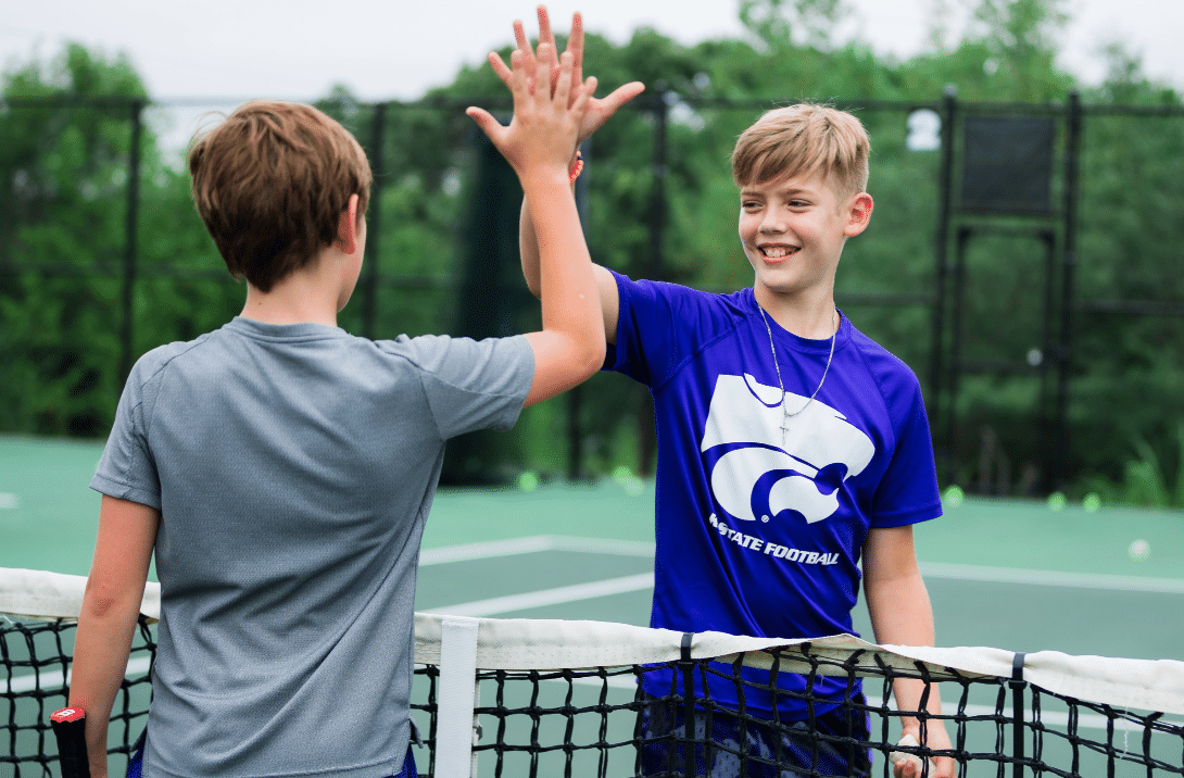 Two young males high-fiving after tennis match outdoors on tennis court