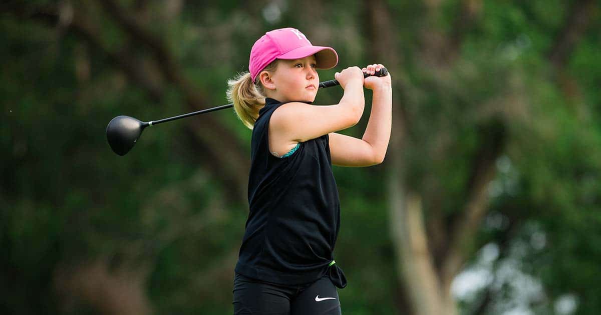 Young girl golfing wearing a black shirt and pink hat