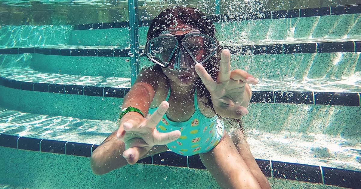 a young girl swimming underwater with goggles on in a pool